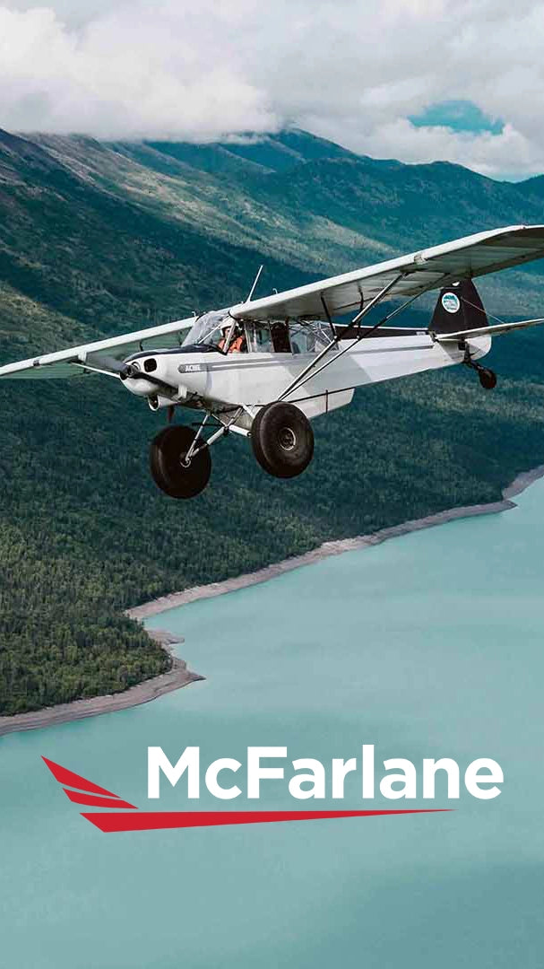 Small airplane flying over a scenic landscape with mountains and water, featuring the McFarlane logo.